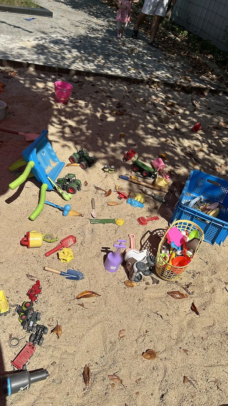 Sand playground scattered with toys and a tractor nearby