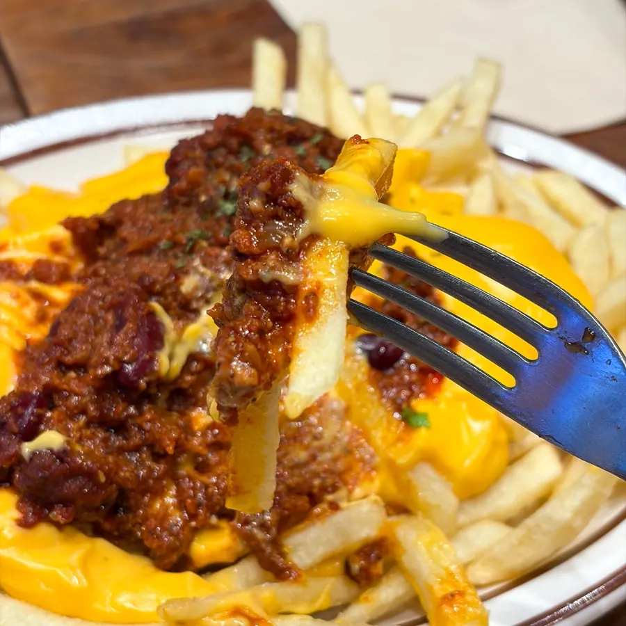 A plate of chili cheese fries mixed with chili sauce and cheese