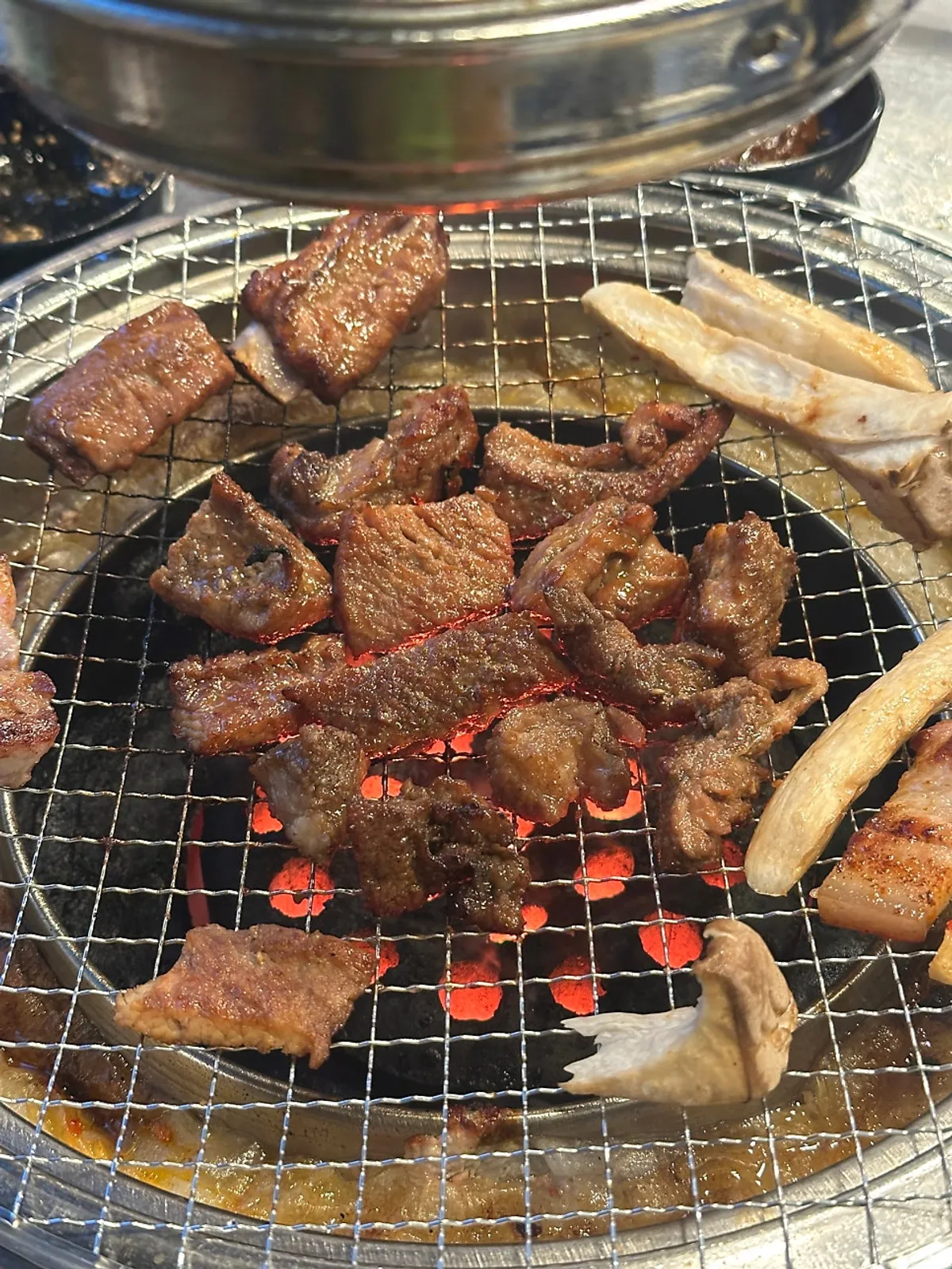 Two pieces of house-marinated pork ribs grilling over charcoal at a time