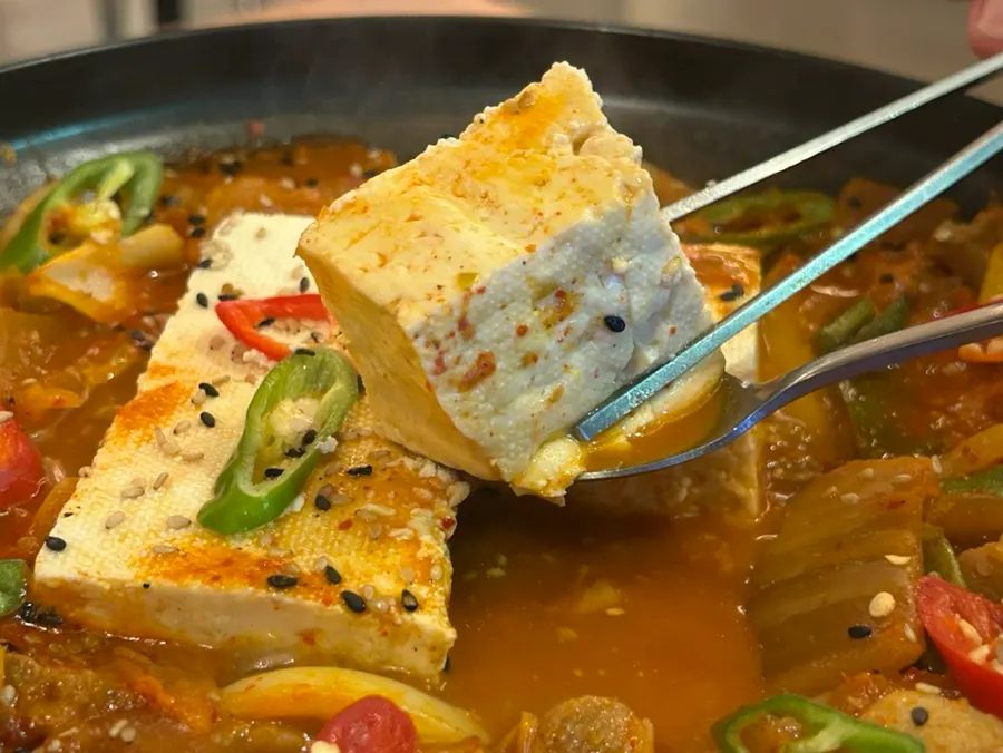 A piece of whole tofu lifted with chopsticks