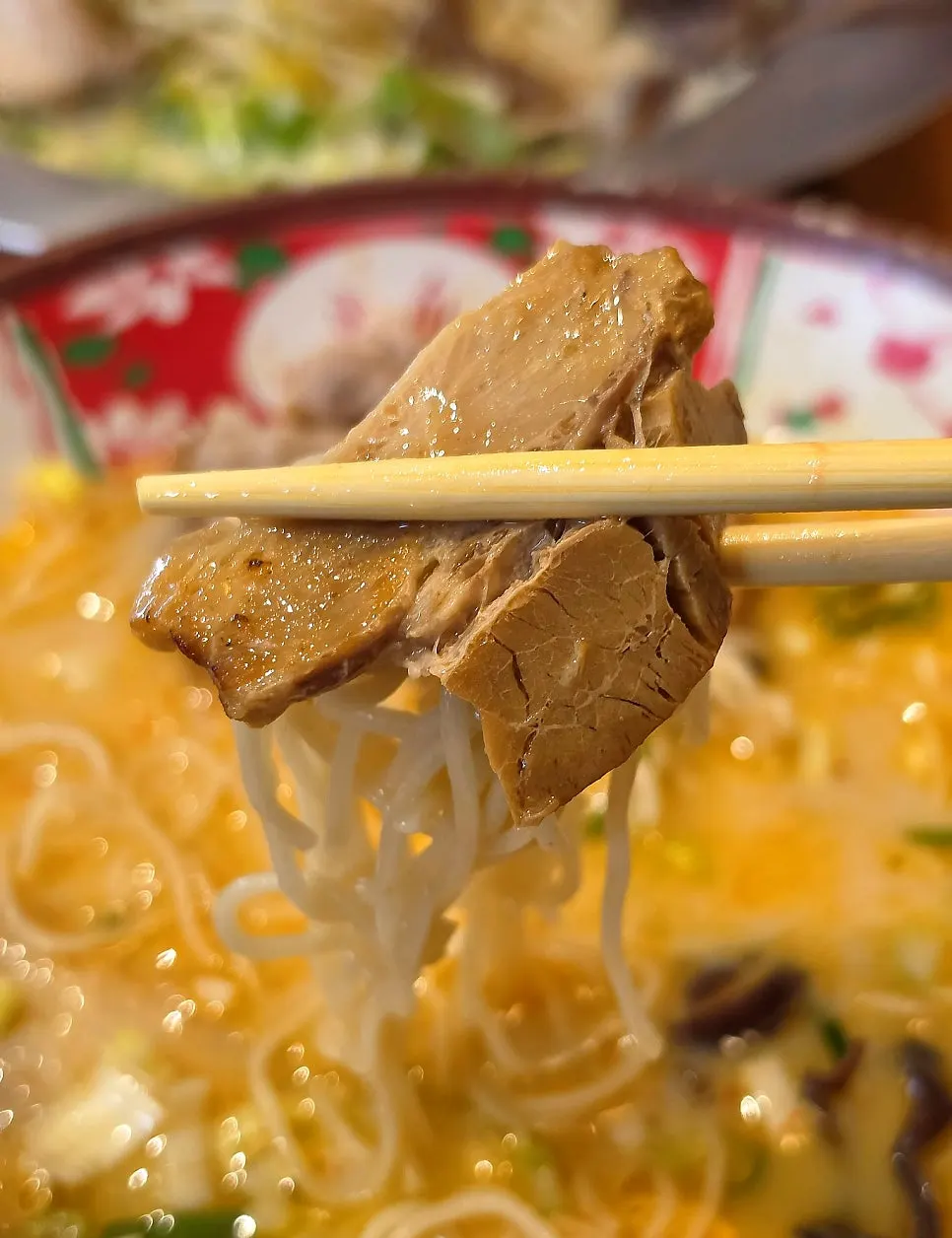 Chopsticks holding char siu wrapped around noodles