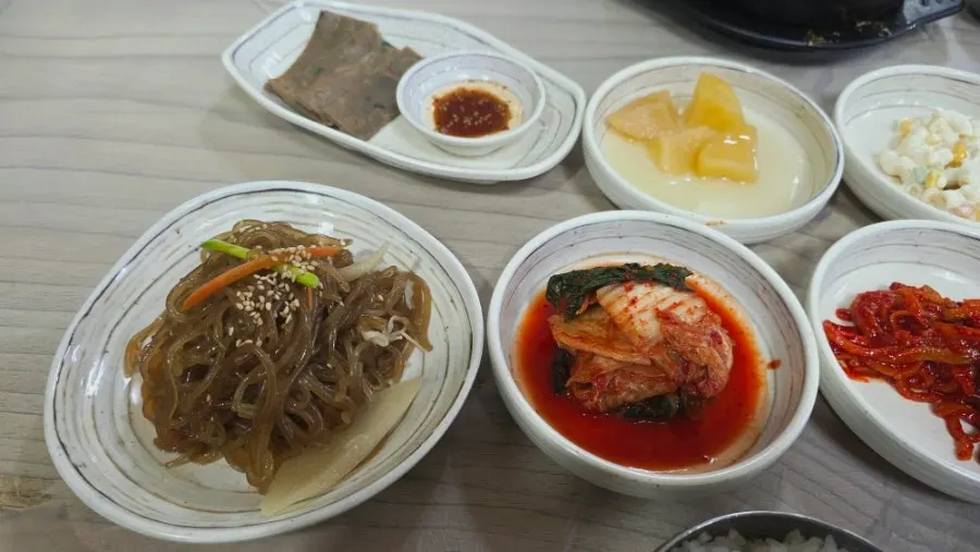 Spread of banchan including japchae, braised potatoes and stir-fried anchovies