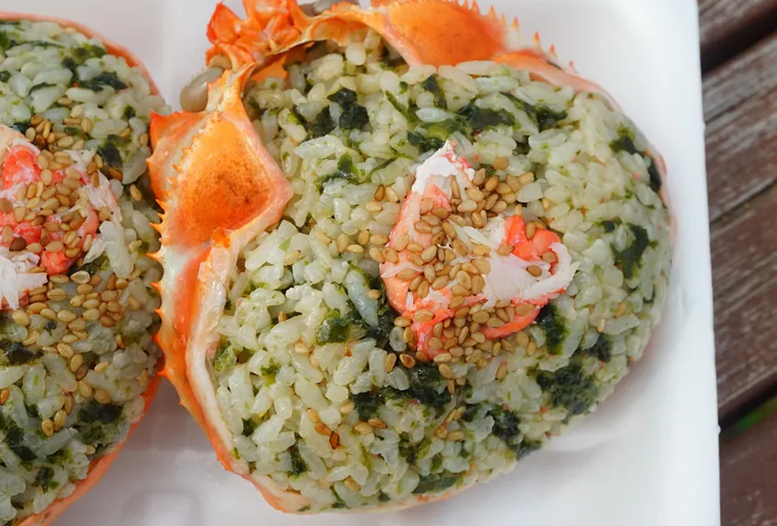 Red snow crab lunchbox and rice ball set unpacked in front of the sea