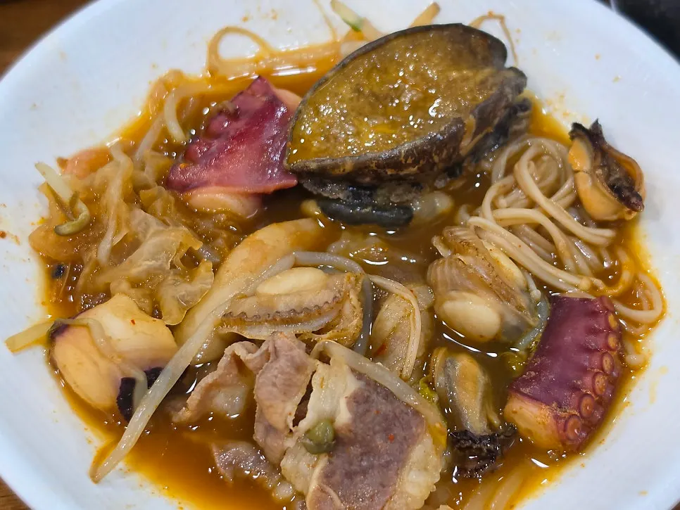Rich seafood jangkalguksu broth scooped up with a ladle