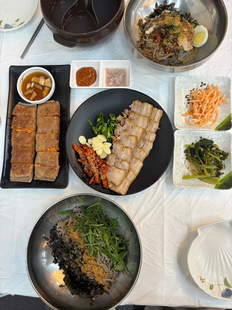 Two bowls of noodles with suyuk and kimchi jeonbyeong on the table