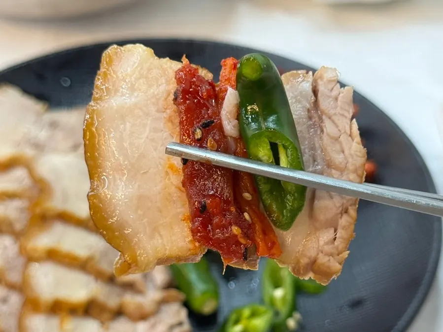 A bite of suyuk topped with seasoned pollack sashimi and dried radish