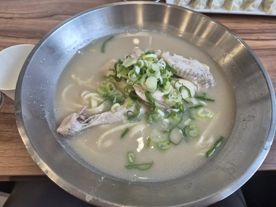 Dak kalguksu in a stainless steel bowl piled with green onion