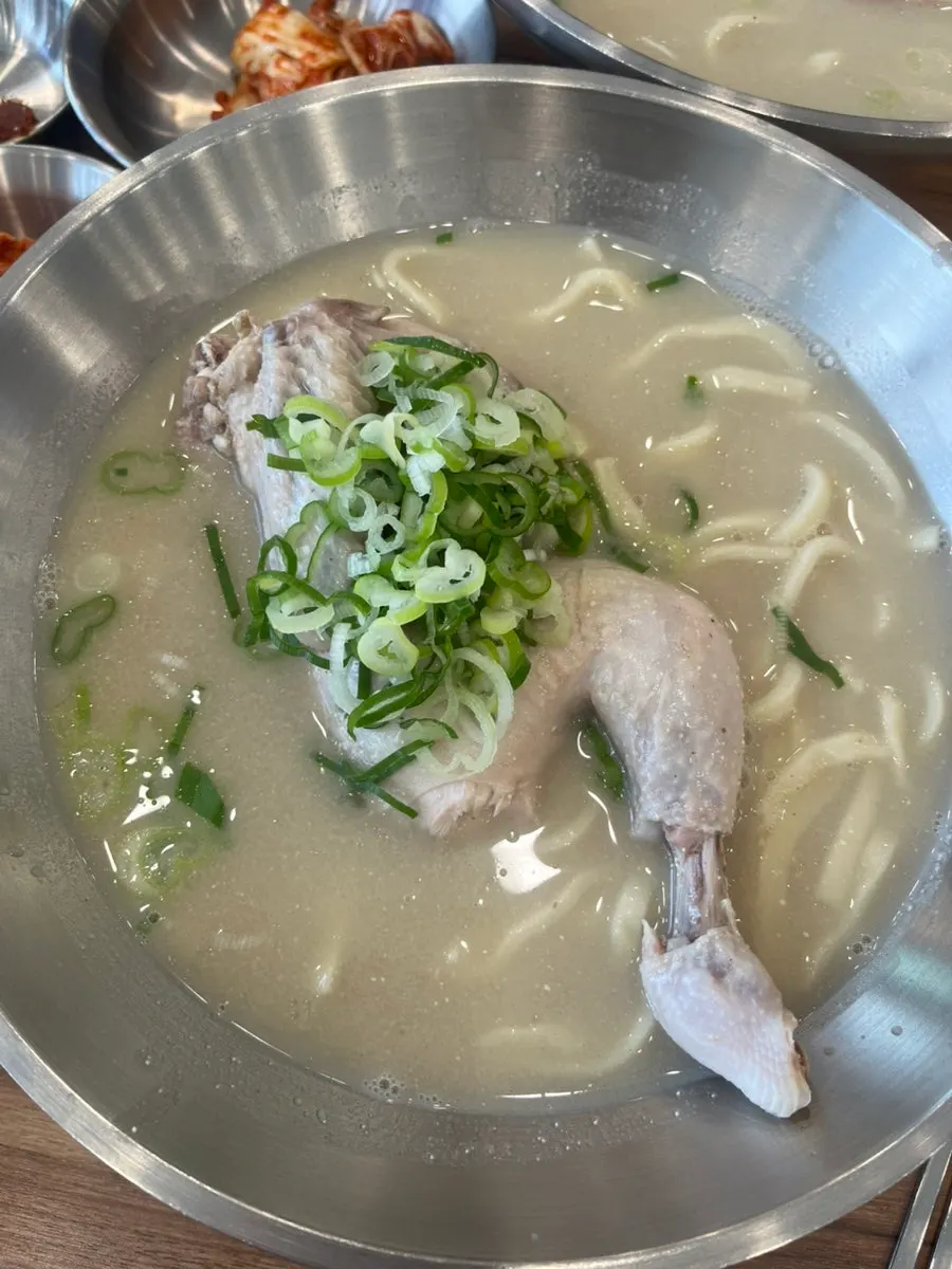 Semangkuk dak kalguksu dengan separuh ekor ayam di atasnya