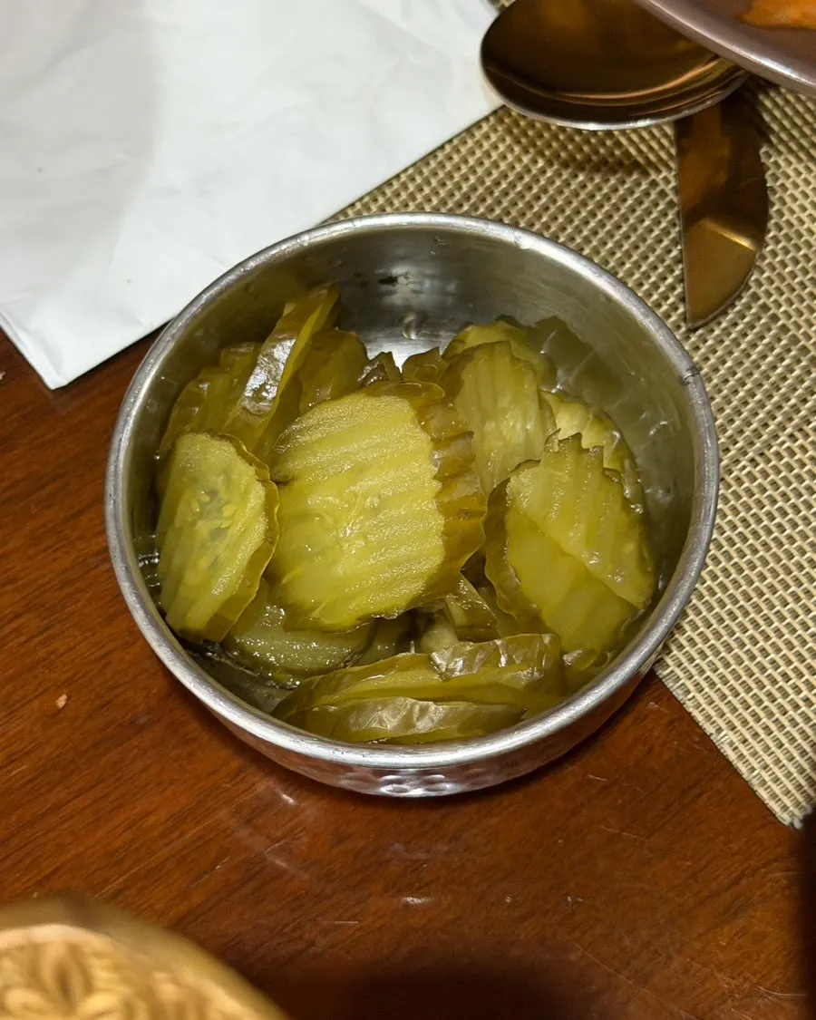 Thinly sliced cucumber pickles in a metal bowl