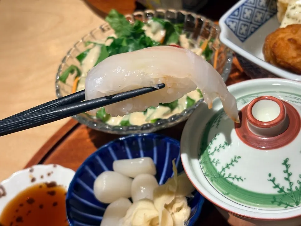 Thick-cut white fish sushi held with chopsticks