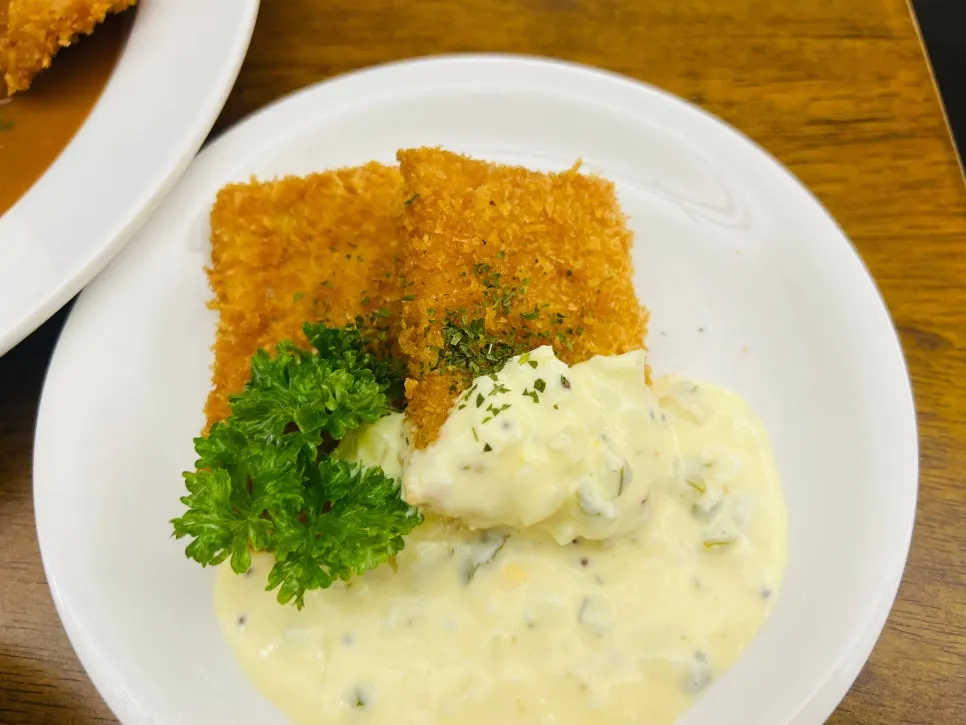 Two pieces of fish cutlet topped with tartar sauce