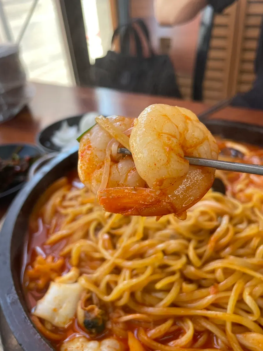 A chopstick-full of jjamppong showing shrimp and squid