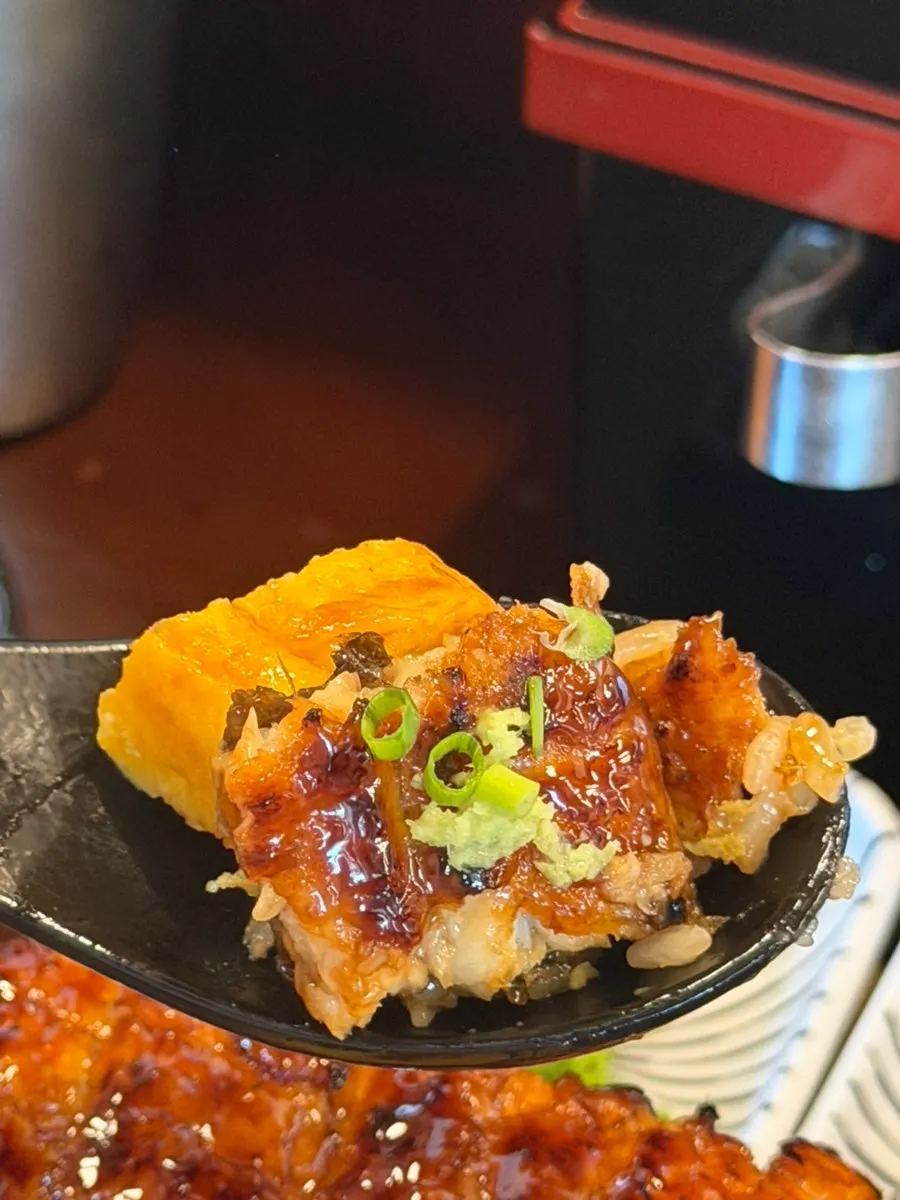 A bite of eel rice bowl topped with wasabi and scallion