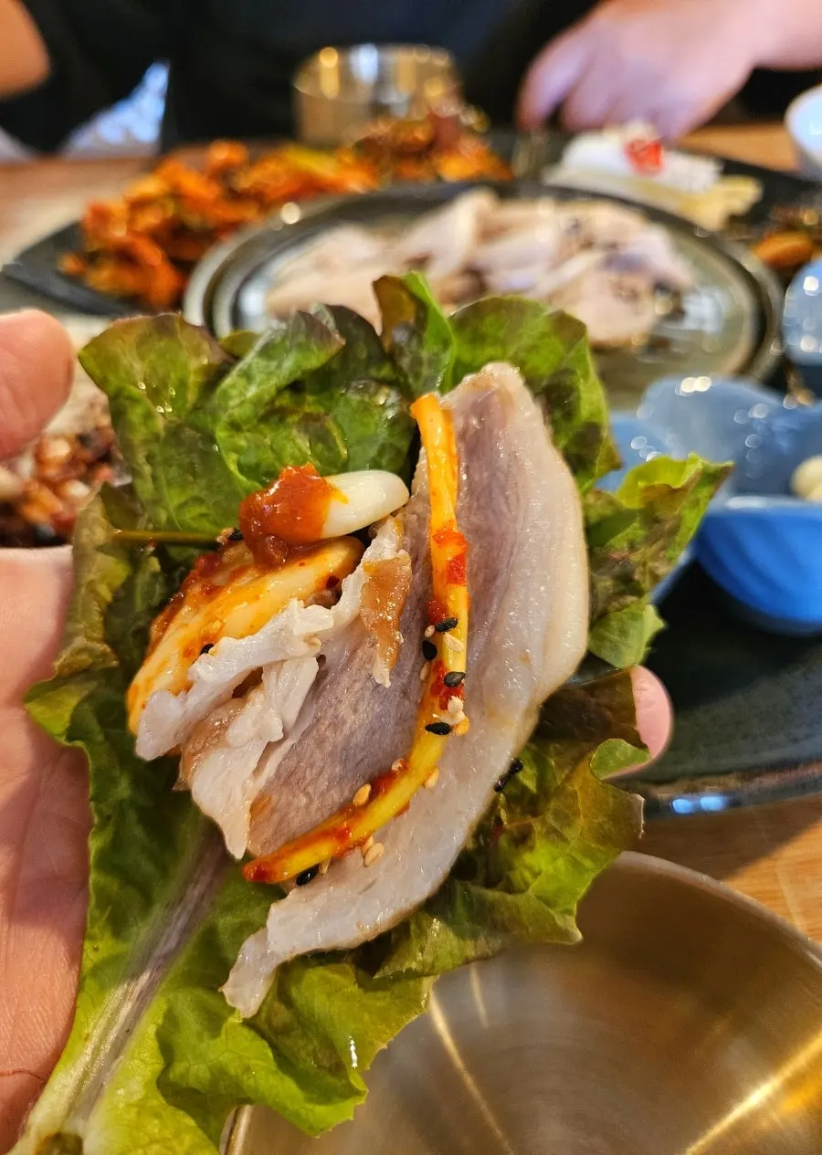 A bite of bossam and ssamjang wrapped in a vegetable leaf