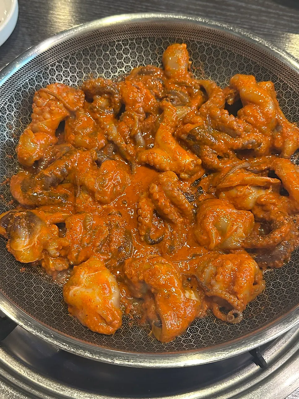 Plump octopus in a shallow pool of red sauce on the griddle