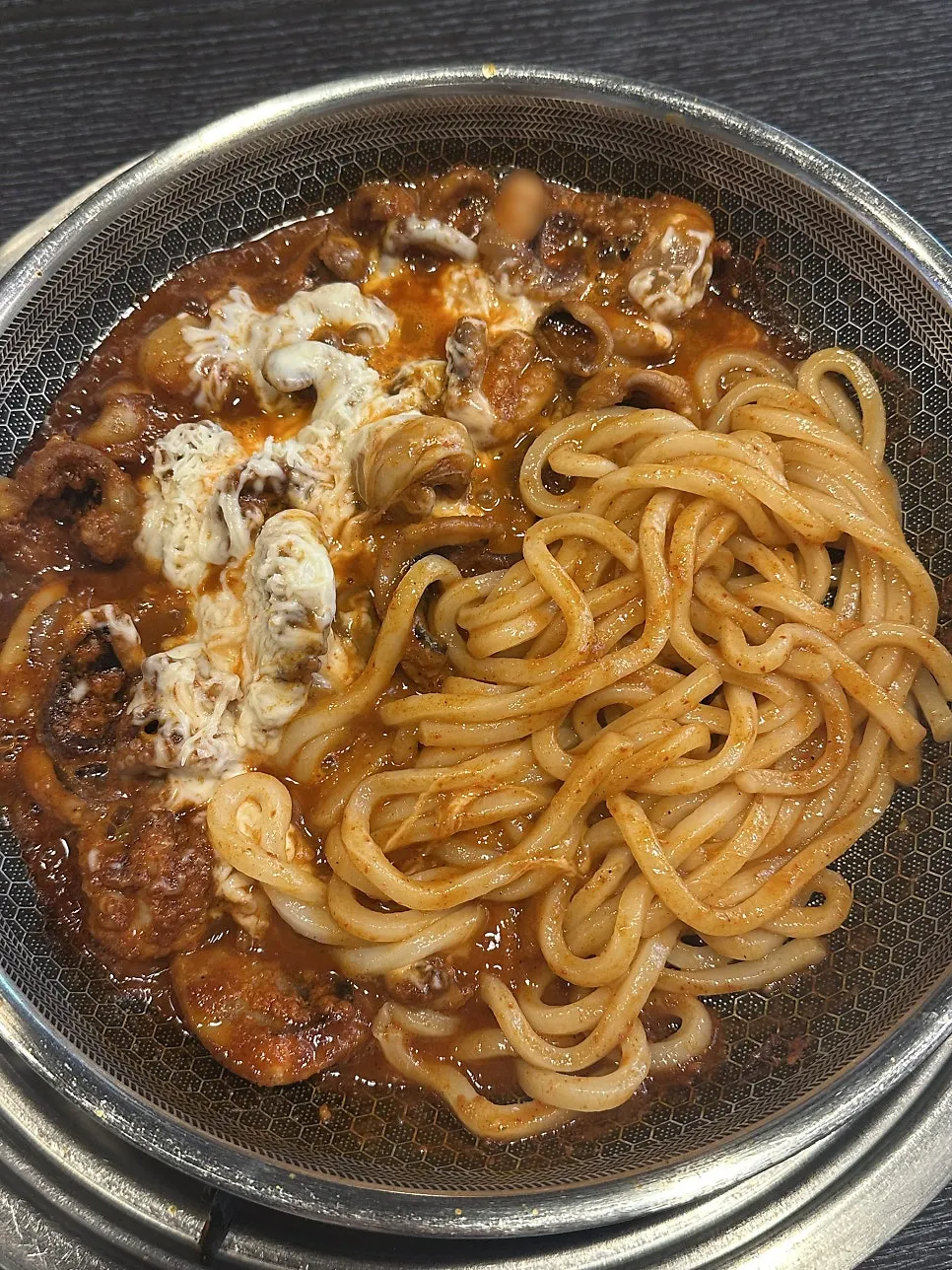 Griddle with melted cheese on one side and sauce-soaked udon noodles on the other