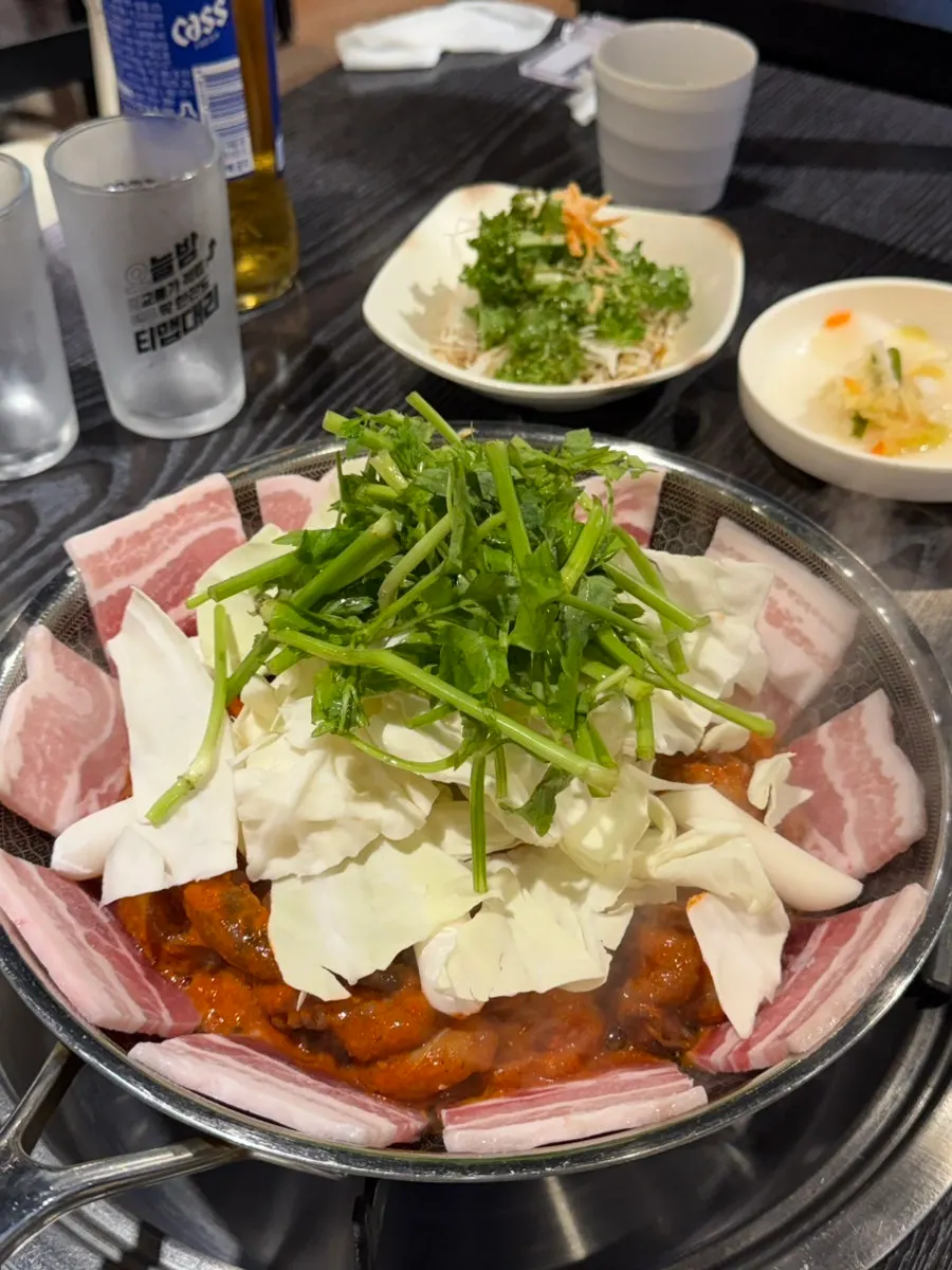 Unlit grill pan with pork belly and noodle add-ins over raw jjukkumi
