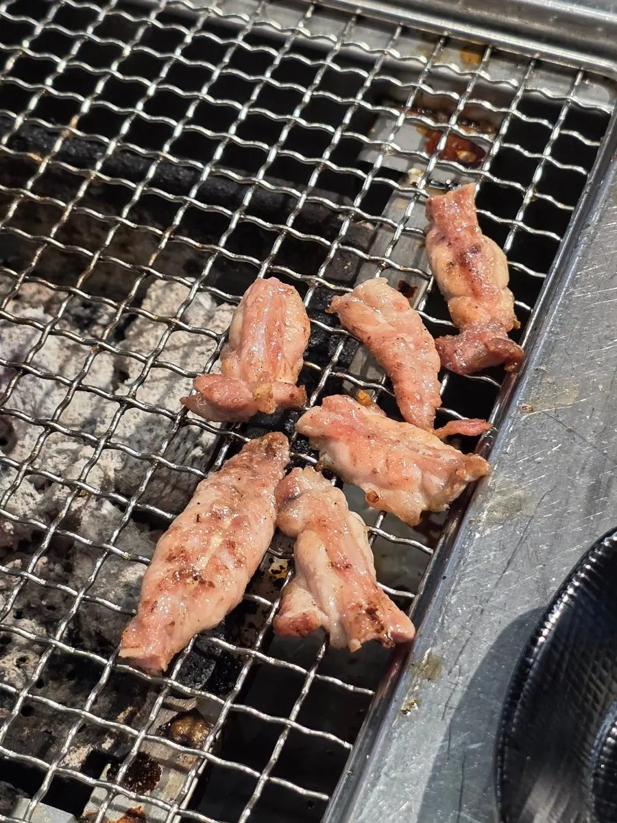 Raw duck neck grilling over charcoal