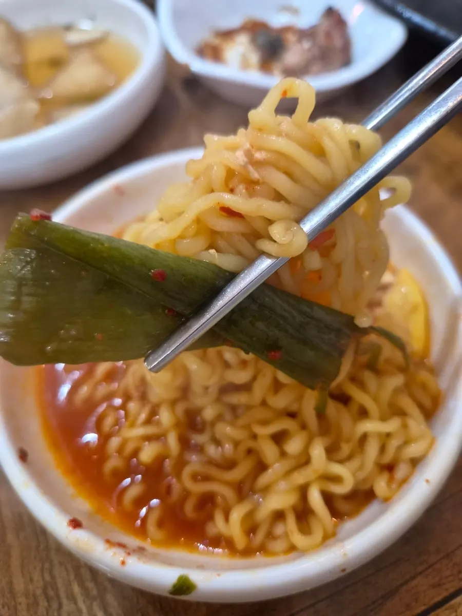 A piece of green onion kimchi placed on top of the ramyeon