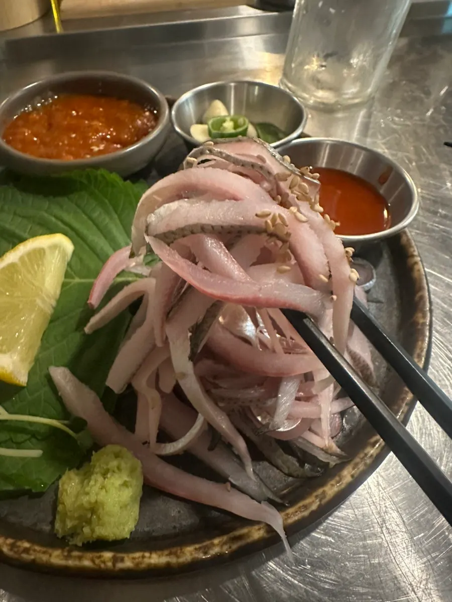 A piece of gizzard shad sashimi dipped in chogochujang