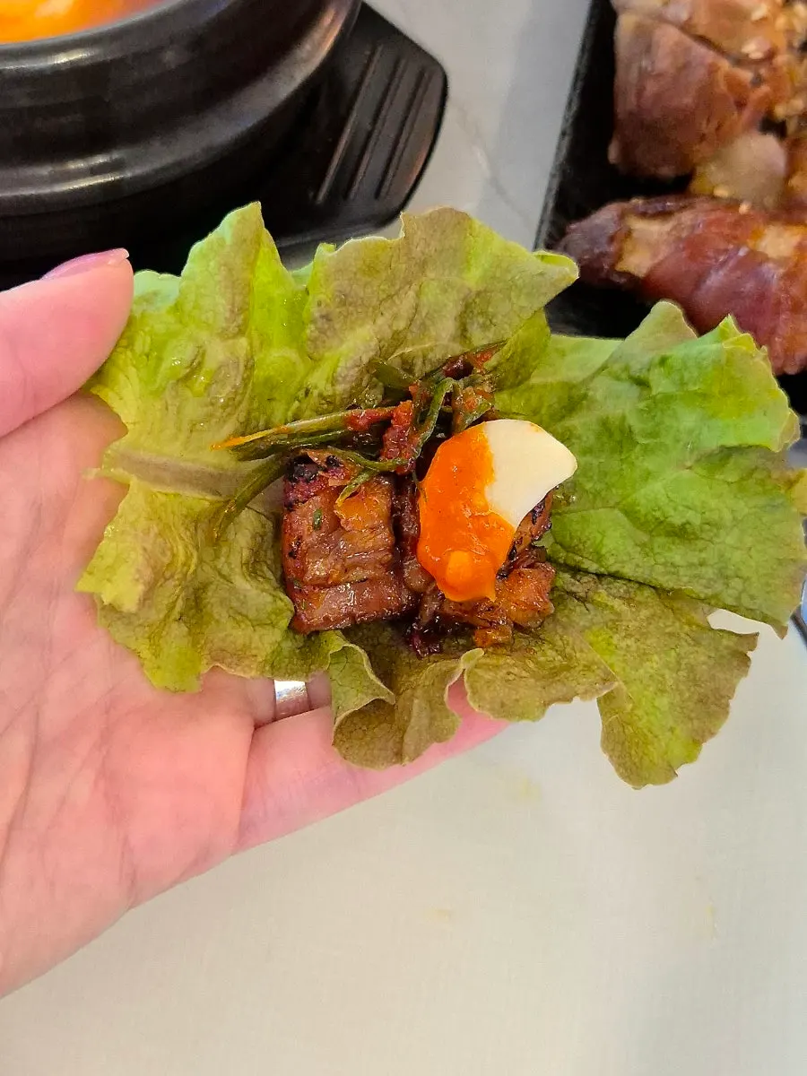 A bite of jokbal with lettuce wrap and salted shrimp