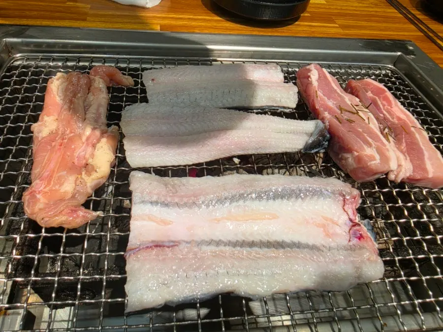 Eel and pork belly grilling together on the charcoal grate