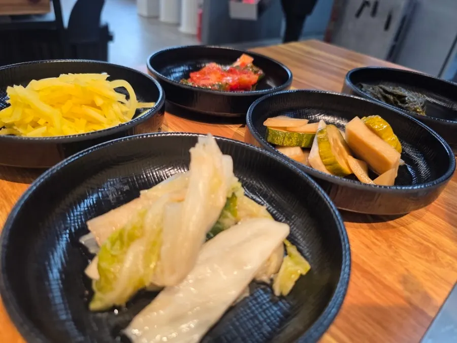 Side dish spread of white kimchi, pickles, green onion kimchi and perilla leaf pickles