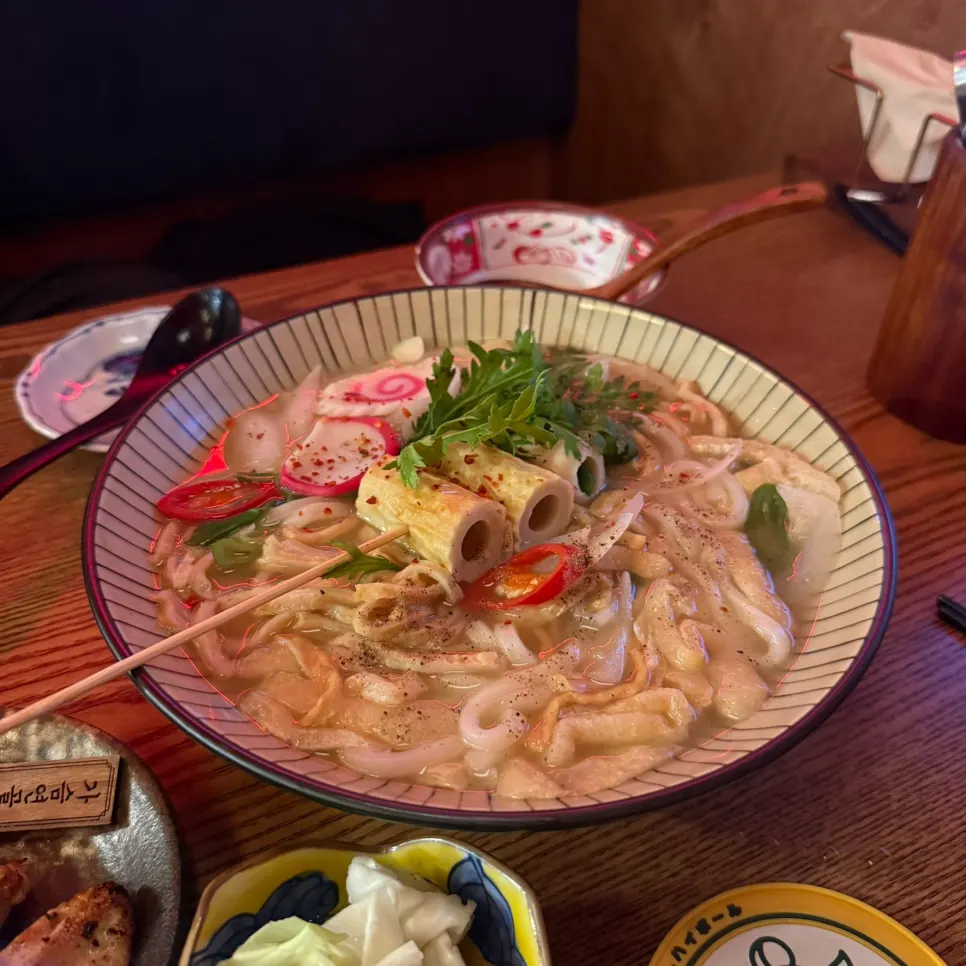 Spicy fishcake udon topped with fishcake, fried tofu, and crown daisy greens