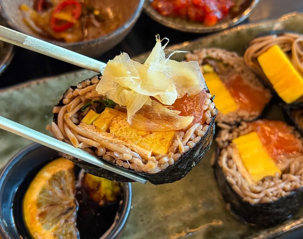 Raw salmon buckwheat gimbap being dipped in soy sauce