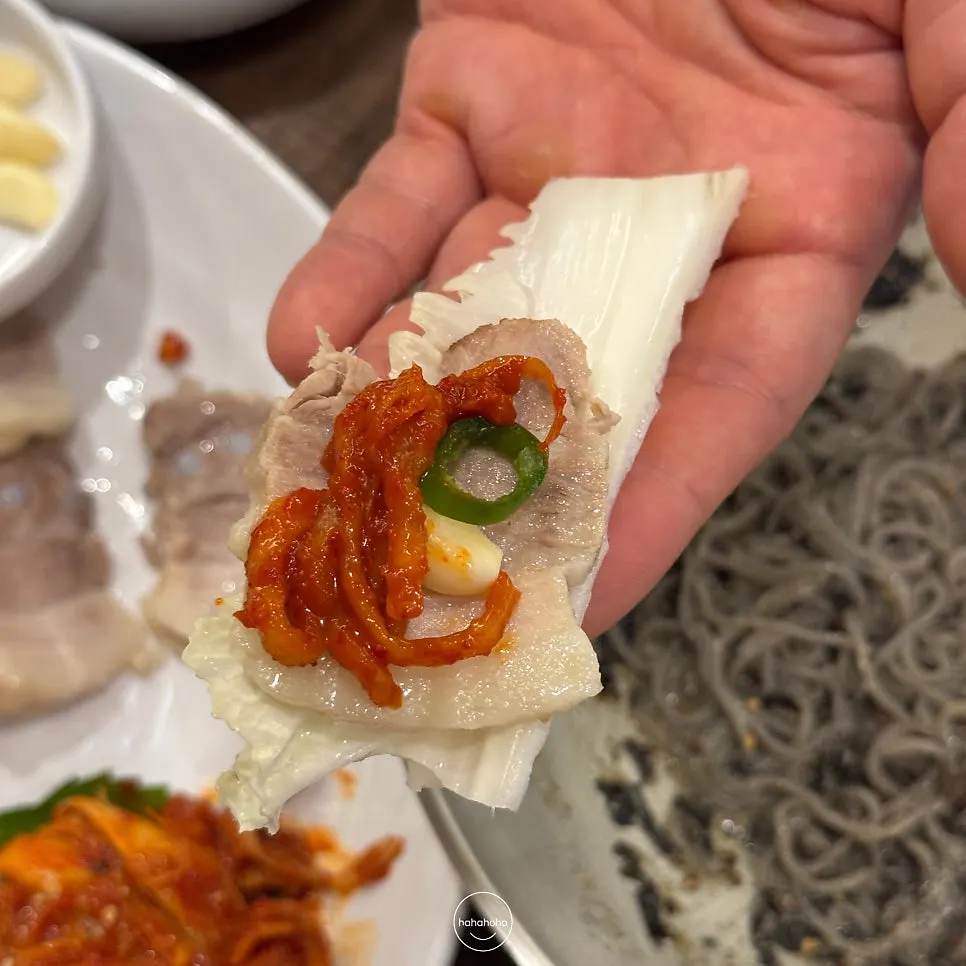 Wrap of young napa cabbage topped with boiled pork and accompaniments