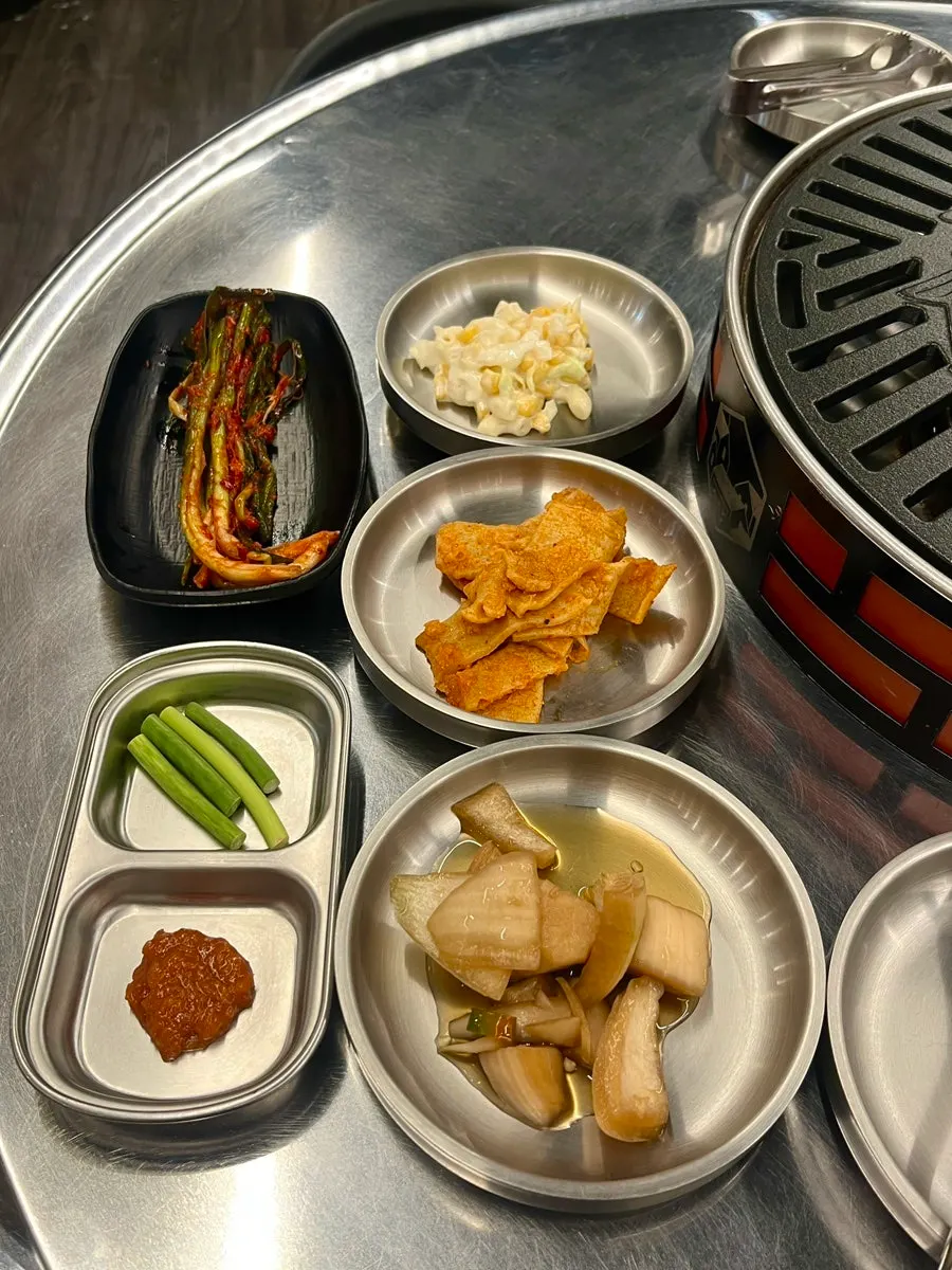 A spread of basic side dishes including green onion kimchi and corn salad