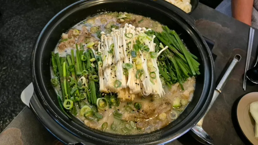 Tendon hot pot topped with chives and enoki mushrooms