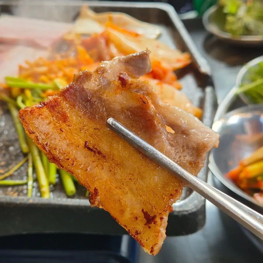 Meat grilling alongside kimchi and bean sprouts on the grill