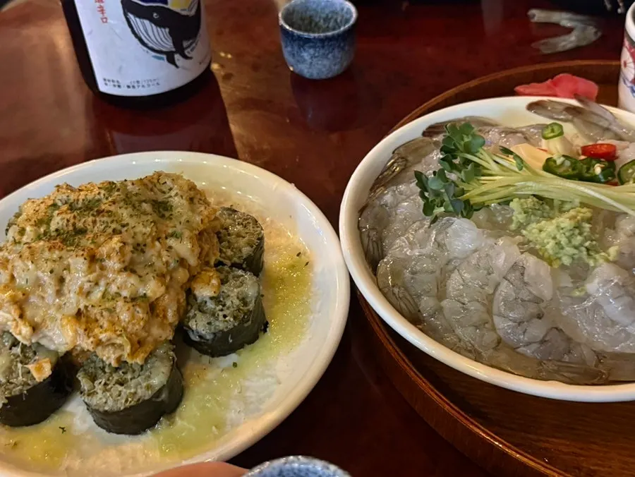 A bite of ankimo maki topped with raw shrimp sashimi