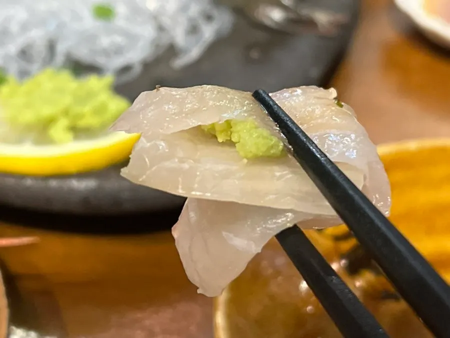 A piece of flounder sashimi dipped in soy sauce