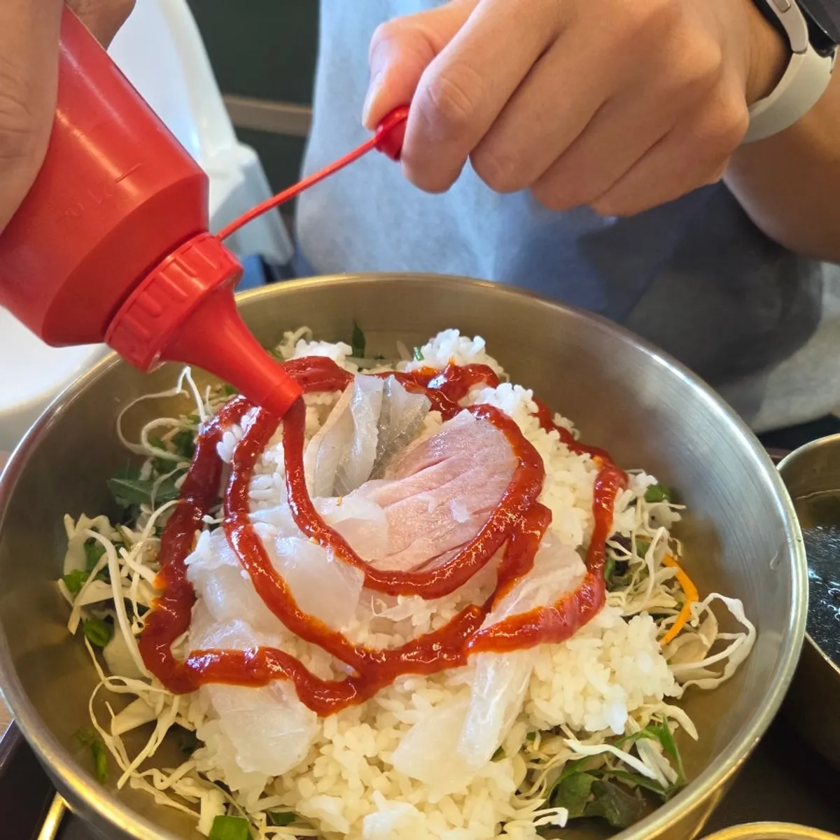 Rice and sashimi being added to the bowl for bibimbap