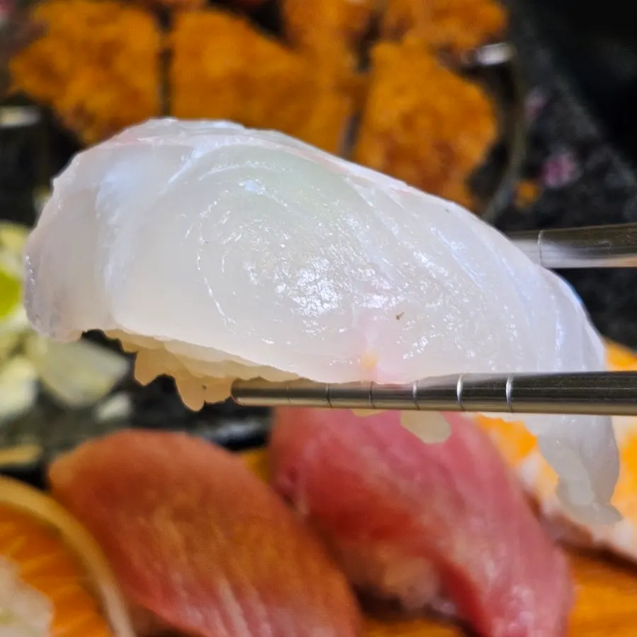 Salmon sushi topped with onion and sauce next to tuna sushi