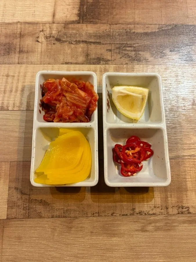 Side dishes of kimchi, pickled radish, chili, and lemon