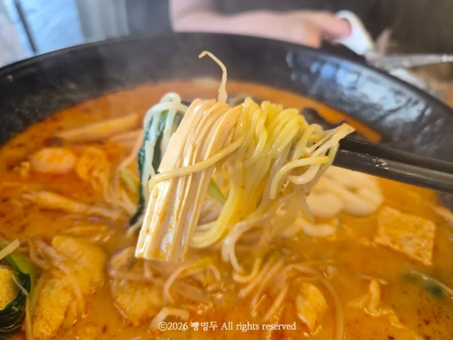 A chopstick bite of malatang with corn noodles and enoki mushrooms