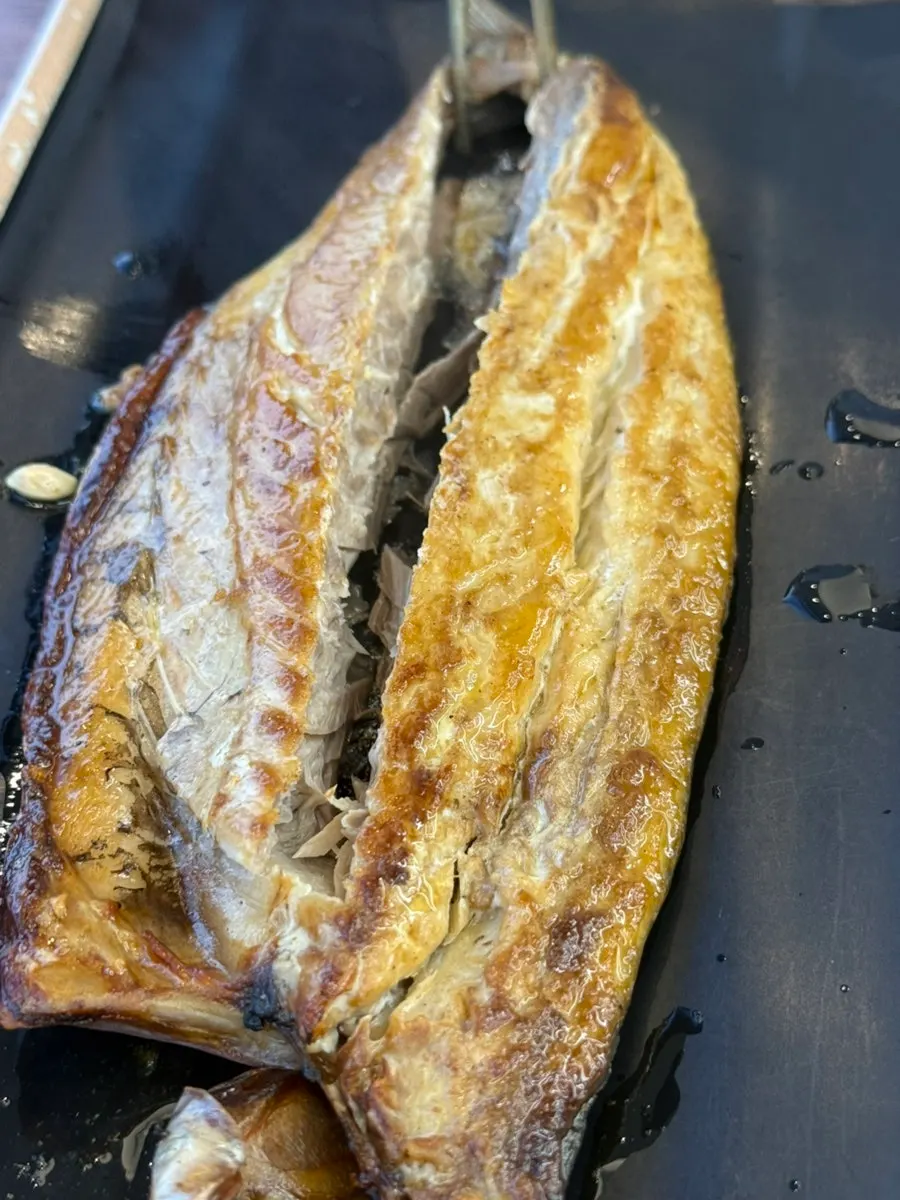 A piece of grilled fish held with chopsticks