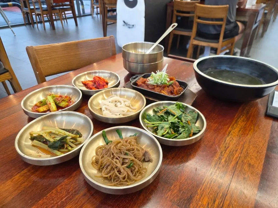 Table spread of standard side dishes including namul and japchae