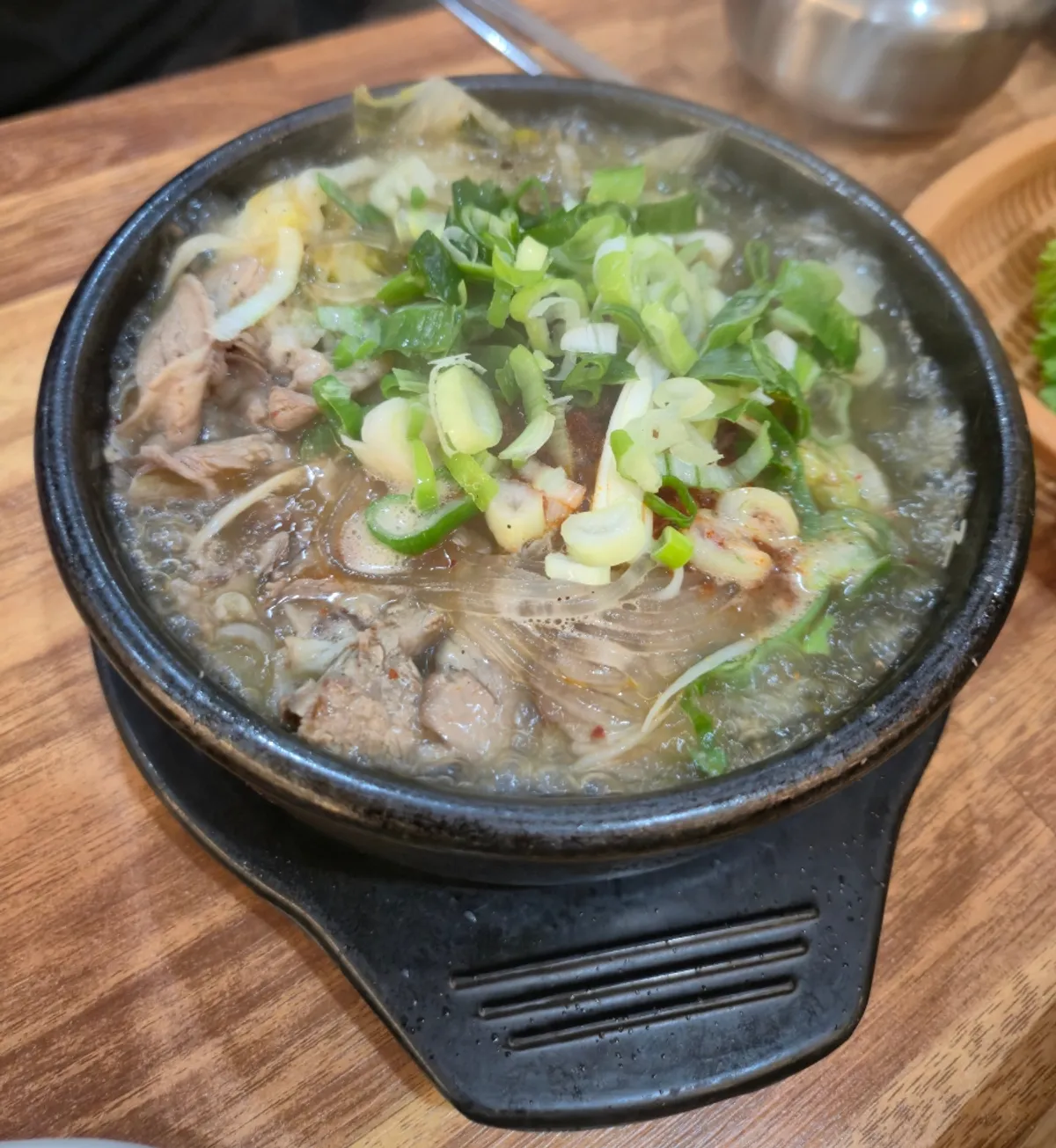 Stone pot of hangover soup topped with scallions and dried greens