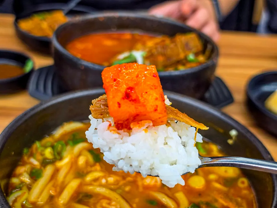 A spoonful of rice mixed into spicy broth topped with meat