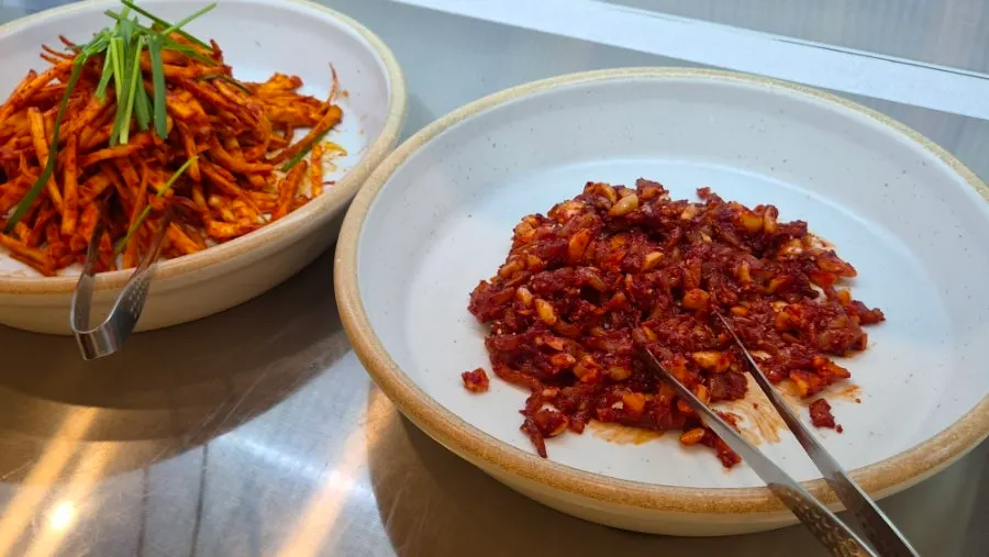 Bibimbap vegetables and side dishes laid out at the self-serve bar