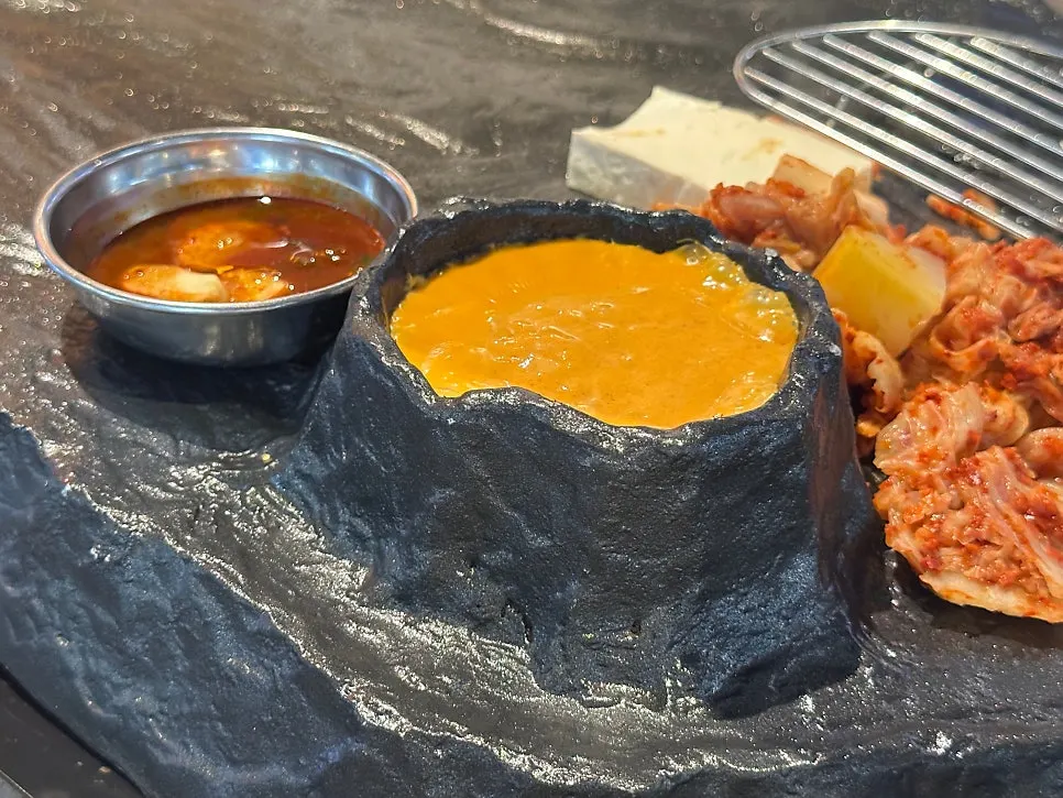 Meat grilling on the stone plate alongside bubbling lava fondue cheese