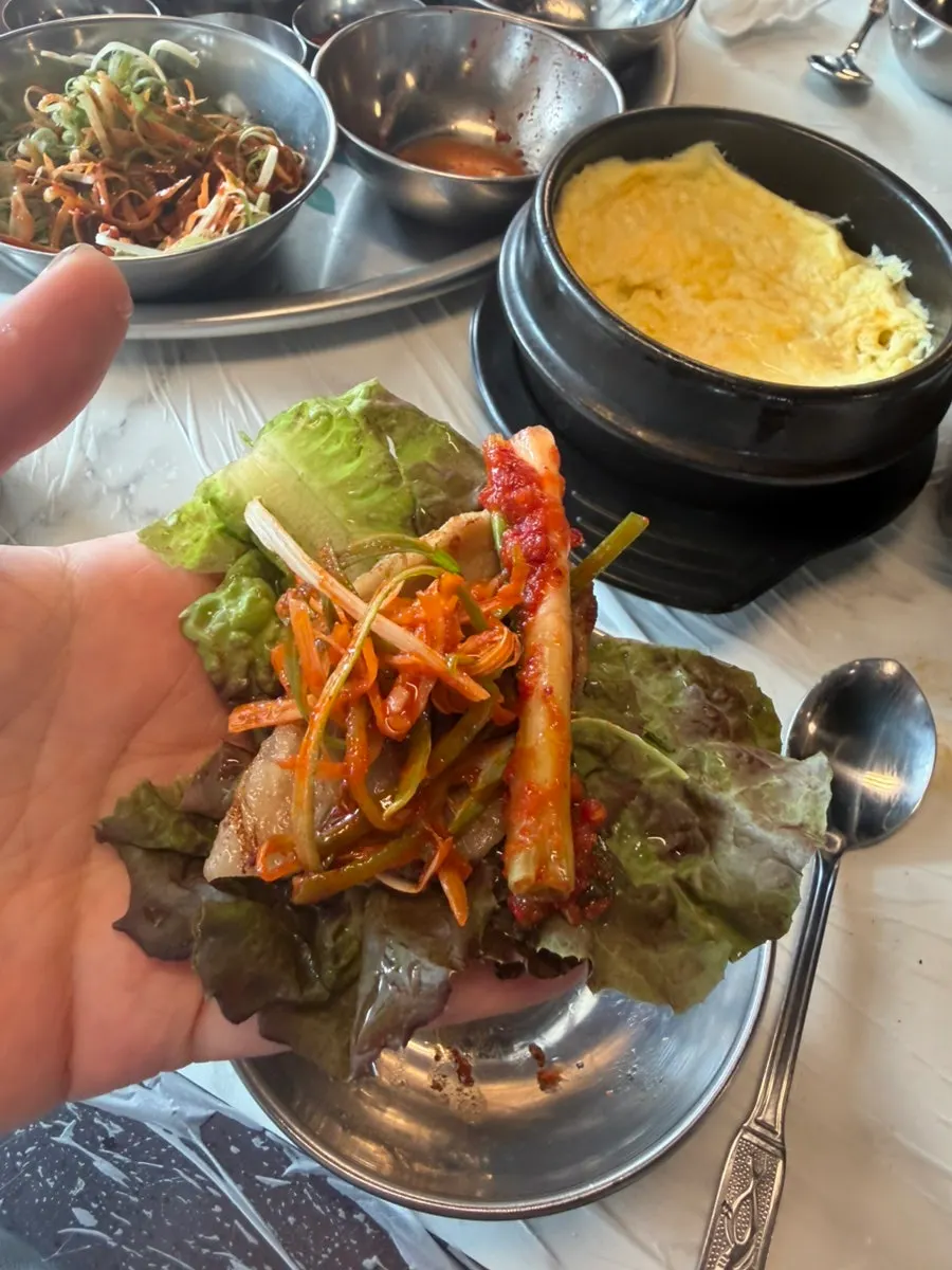 A lettuce wrap with meat, kimchi, and bracken