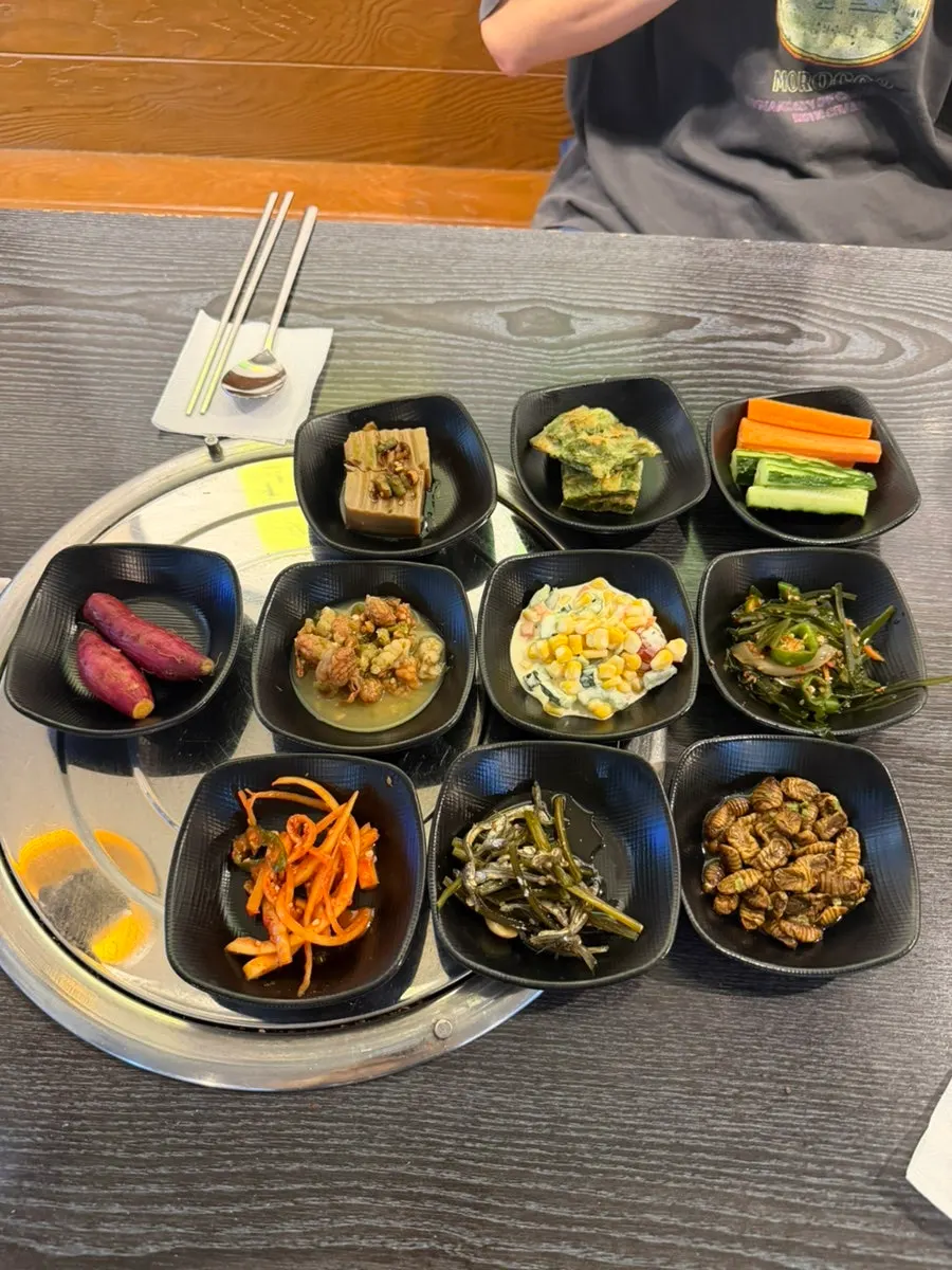 A spread of side dishes including acorn jelly, chive pancake, and silkworm pupae