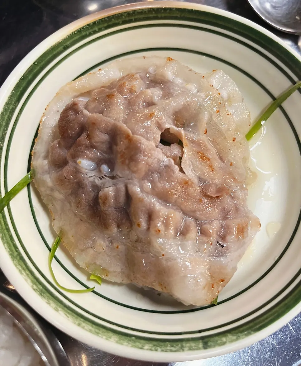Thin pork belly grilling on a tilted stone plate with onion and garlic