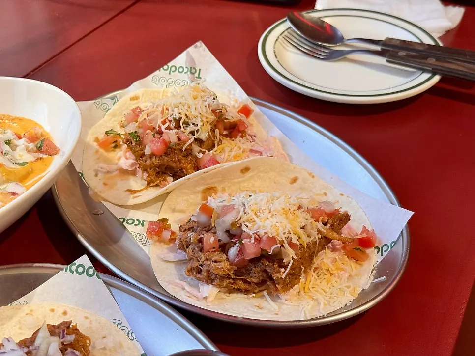 Two pieces of pulled pork taco topped with tomato and cheese