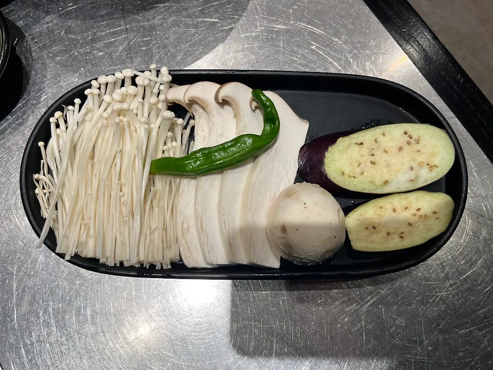Four free sides: jjolmyeon, steamed egg, flat mandu, and mixed mushrooms